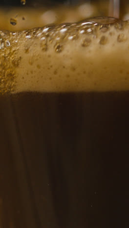 Vertikales-Video-Von-Pint-Irish-Stout,-Das-In-Glas-Vor-Schwarzem-Studiohintergrund-Gegossen-Wird,-Um-Den-St.-Patricks-Day-Zu-Feiern